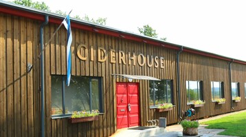Holzgebäude mit roter Tür, beschriftet "Ciderhouse", blumengeschmückte Fensterbänke und estnische Flagge.