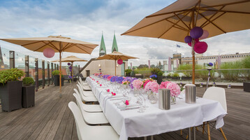 Festlich gedeckter Tisch auf der Dachterrasse des ATLANTIC Grand Hotel Bremen mit Blumen und Sonnenschirmen.
