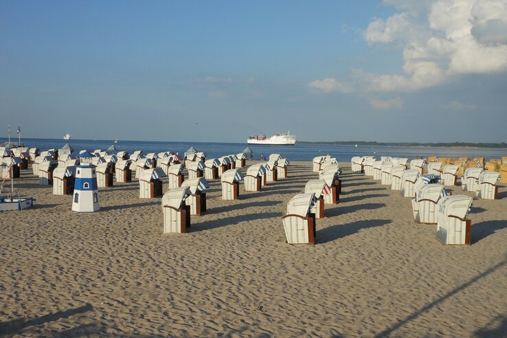 Beach chairs on the sandy beach of Travemünde with a view of the Baltic Sea and passing ships.