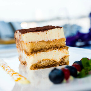 Tiramisu auf weißem Teller, dekoriert mit Beeren und Minzblättern, im ATLANTIC Hotel Galopprennbahn Bremen.