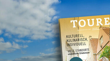 A magazine with travel motifs floats above a vast, cloudy tidal flat landscape.