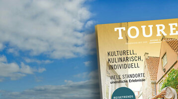 Ein Magazin mit Reisemotiven schwebt über einer weiten, bewölkten Wattlandschaft.