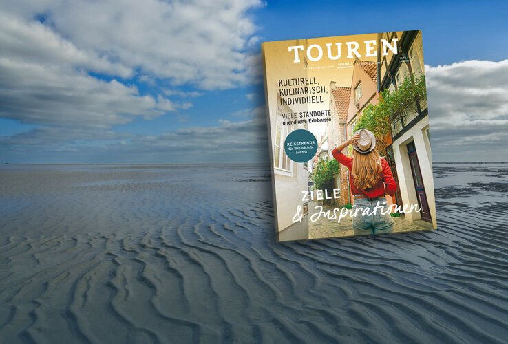 A magazine with travel motifs floats above a vast, cloudy tidal flat landscape.