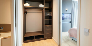 Modern hotel room hallway with open closet, safe, bathroom on the left and view into the bedroom with TV.