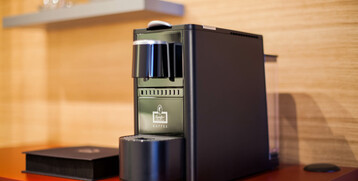 Kaffeemaschine auf rotem Regal im ATLANTIC Hotel Airport Bremen, mit Tassen im Hintergrund.