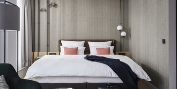 Modernes Hotelzimmer mit Doppelbett, stilvoller Beleuchtung, Sessel und Tisch mit Brille, Tasse und Zeitschrift.