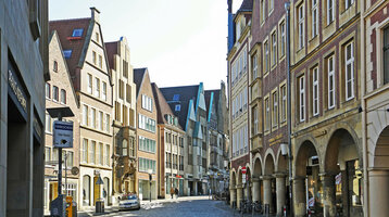 Historische Altstadtstraße in Münster mit Kopfsteinpflaster, umgeben von traditionellen Giebelhäusern und Arkaden.