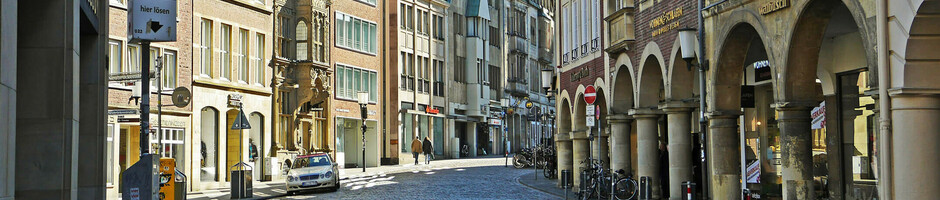 Historische Altstadtstraße in Münster mit Kopfsteinpflaster, umgeben von traditionellen Giebelhäusern und Arkaden.