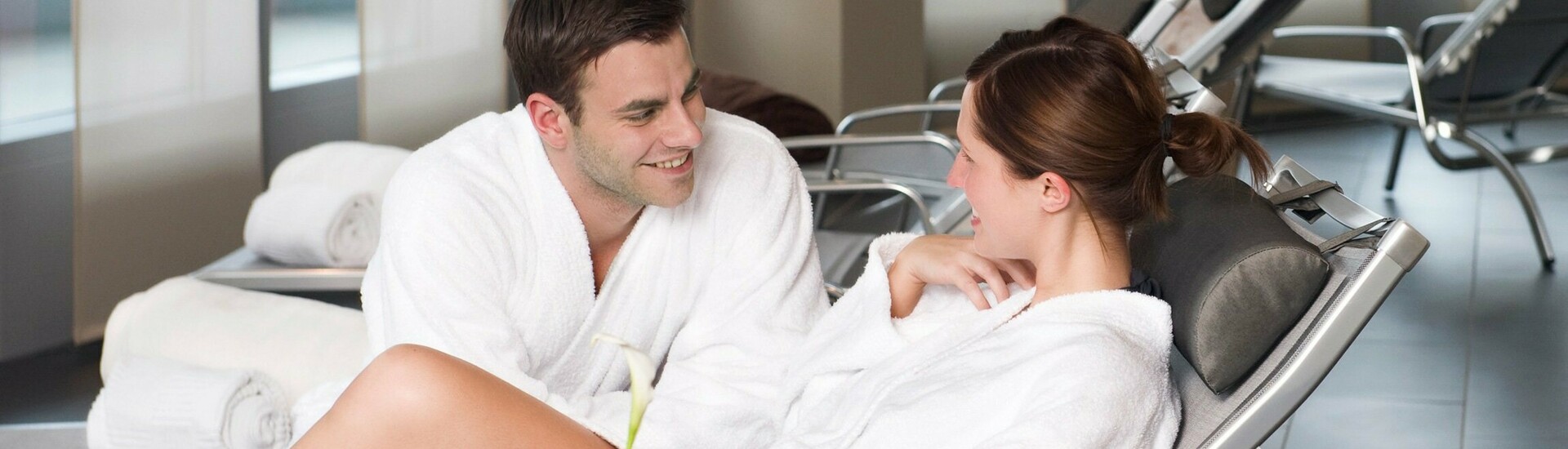 Couple in bathrobes relaxing on loungers in the hotel's modern spa area.
