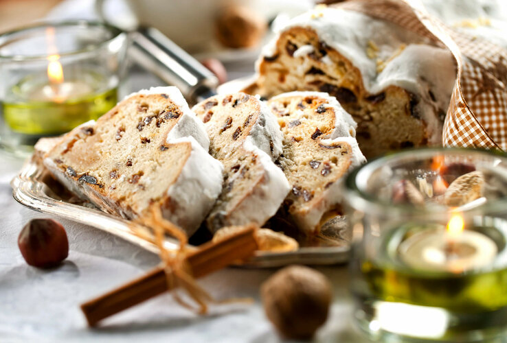 Stollen with raisins and powdered sugar on a plate, surrounded by lighted tea lights and cinnamon sticks.