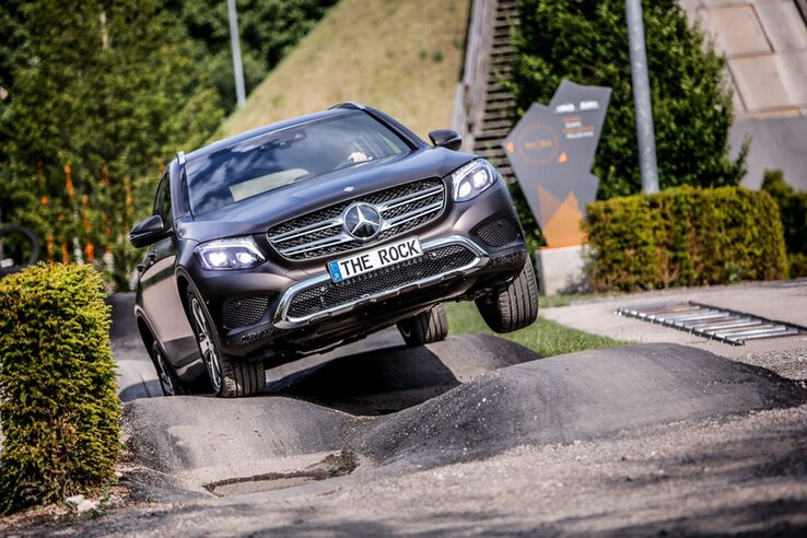 An SUV negotiates an uneven outdoor test track surrounded by trees and signs.