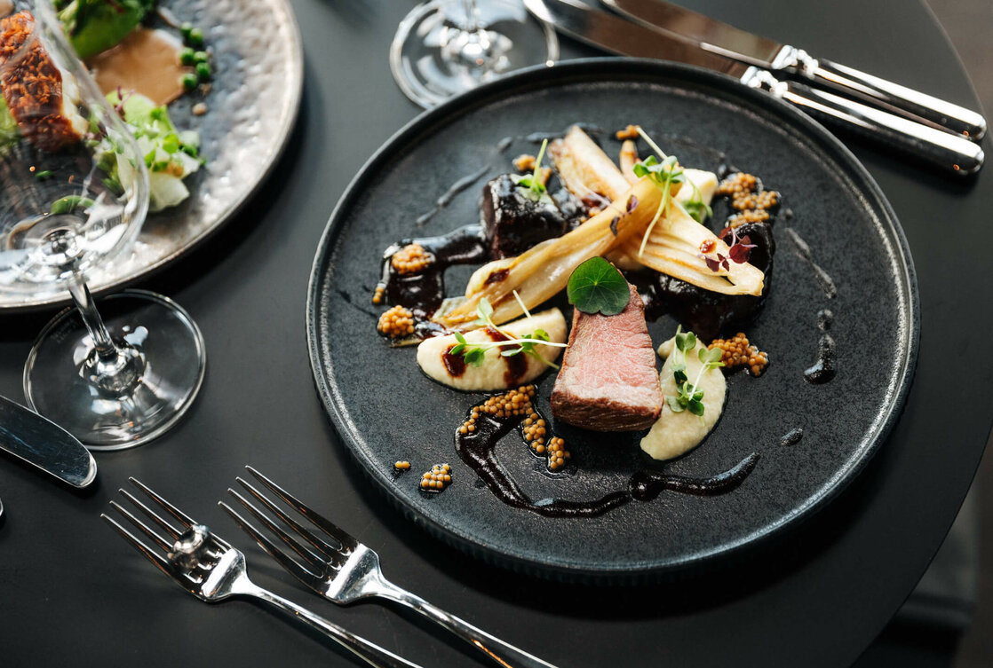 Gourmetgericht auf schwarzem Teller, kunstvoll angerichtet mit Fleisch, Gemüse und Saucen im ATLANTIC Hotel Heidelberg.
