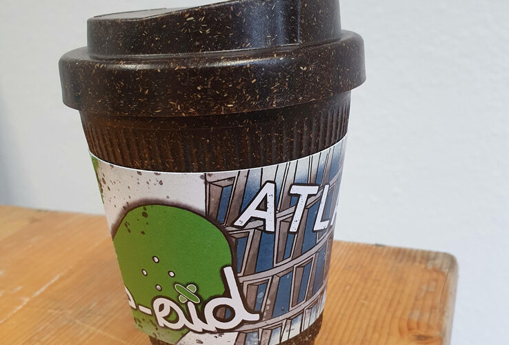 Reusable coffee mug with ATLANTIC Hotel logo on a wooden table.