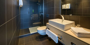 Modern bathroom in the ATLANTIC Hotel Sail City with shower, washbasin, WC and towels on dark tiles.