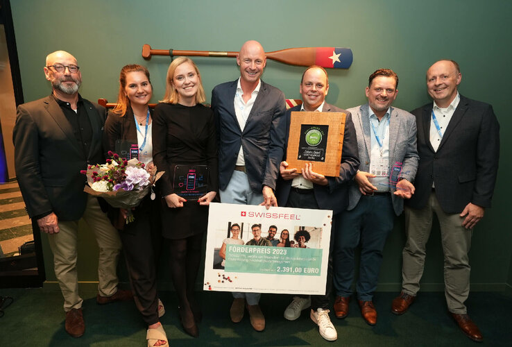 Eine Gruppe von sieben Personen hält Auszeichnungen und Blumen in einem Hotel in Bremerhaven.