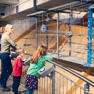 Besucher des Universum Bremen Familie betrachtet interaktive Ausstellung im Universum Bremen, mit komplexen Metallstrukturen und bunten Elementen.