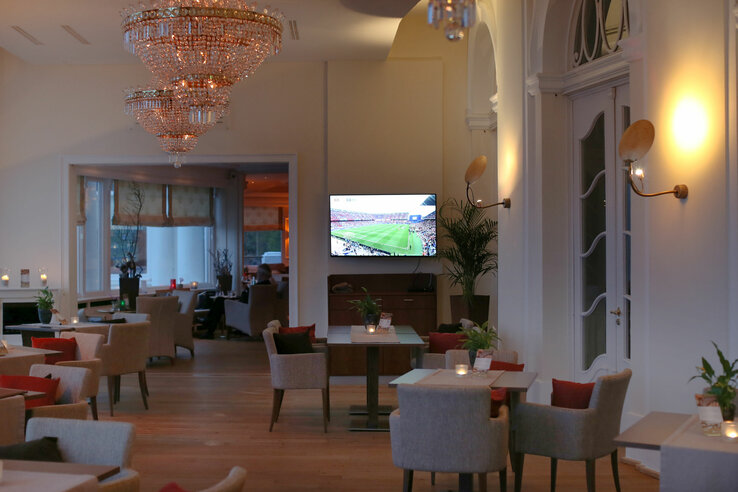 Eleganter Lounge-Bereich im ATLANTIC Grand Hotel mit Kronleuchtern, gemütlichen Sitzgruppen und einem Fernseher an der Wand.