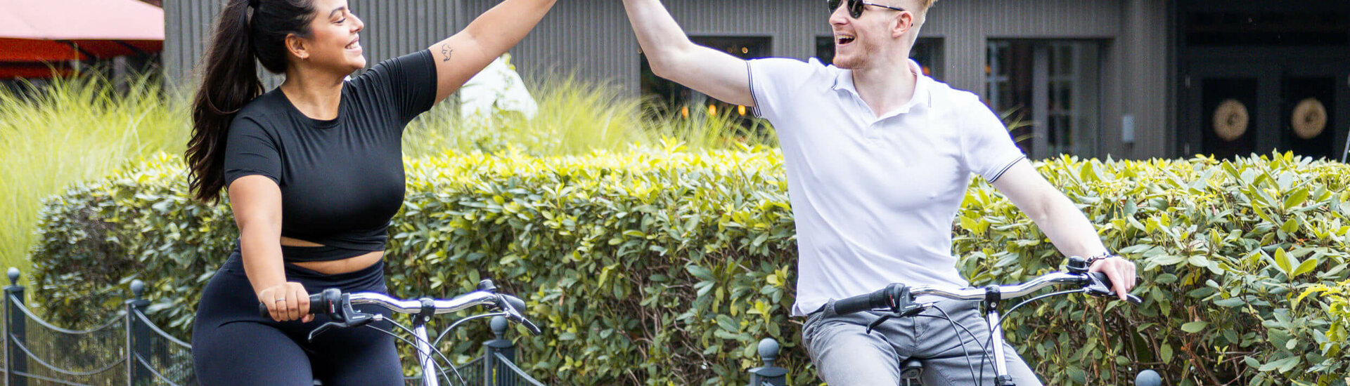 Zwei Personen auf Fahrrädern geben sich vor dem ATLANTIC Hotel Landgut Horn fröhlich ein High-Five.