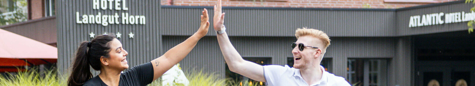 Zwei Personen auf Fahrrädern geben sich vor dem ATLANTIC Hotel Landgut Horn fröhlich ein High-Five.