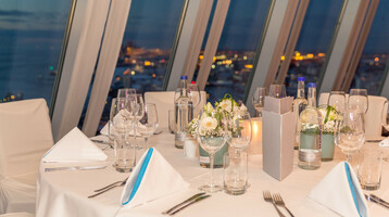 Elegant table setting at the ATLANTIC Hotel Sail City with a view of Bremerhaven at night.