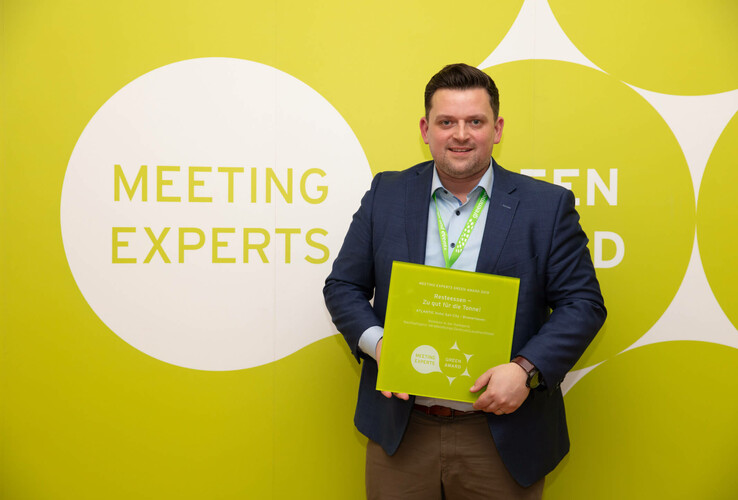 Person with green award in front of yellow wall with "Meeting Experts" lettering in the ATLANTIC Hotel Sail City.