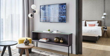 Modernes Hotelzimmer mit Doppelbett, Fernseher, dekorativen Tischen und hellem Vorhang im ATLANTIC Hotel Münster.