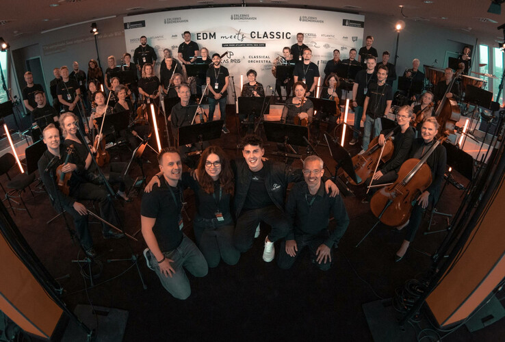 Konzert im ATLANTIC Hotel Sail City Orchester und Crew posieren im ATLANTIC Hotel Sail City, Bremerhaven, vor einem "EDM meets Classic"-Banner.