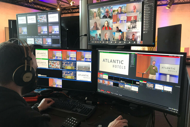 Person steuert Videokonferenz mit mehreren Bildschirmen, "Atlantic Hotels" Logo sichtbar.