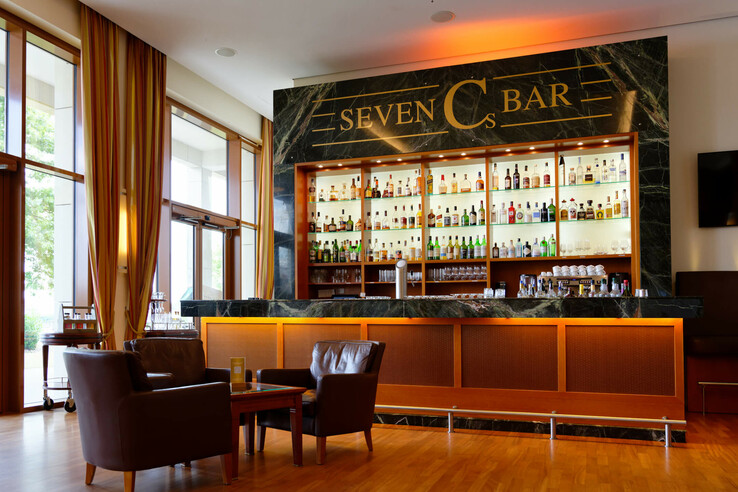 Hotelbar mit elegantem Design, gut bestückten Regalen, Ledersesseln und großen Fenstern mit Vorhängen.