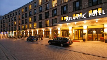 Exterior view of the ATLANTIC Hotel Lübeck at dusk, illuminated entrance area, parked cars in front of the hotel.