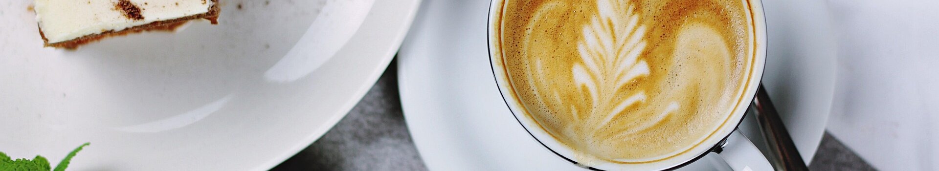 Kaffee mit Latte Art und Dessert auf einem Tisch, daneben Limetten und Minzblätter.
