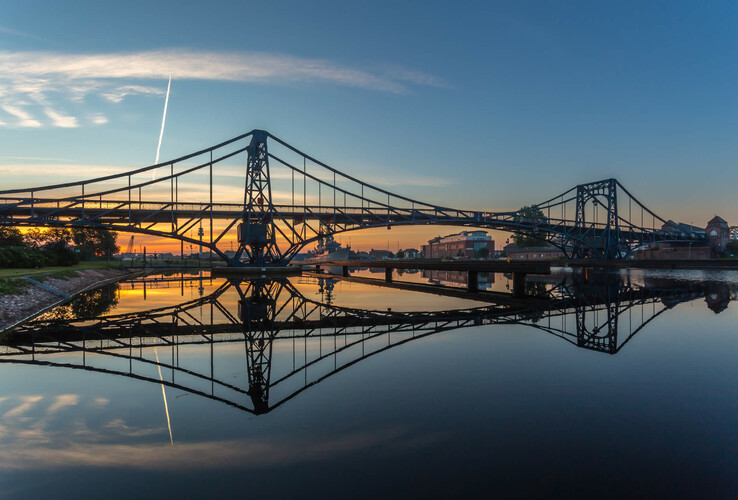 Sonnenuntergang über einer Brücke, die sich im ruhigen Wasser spiegelt.
