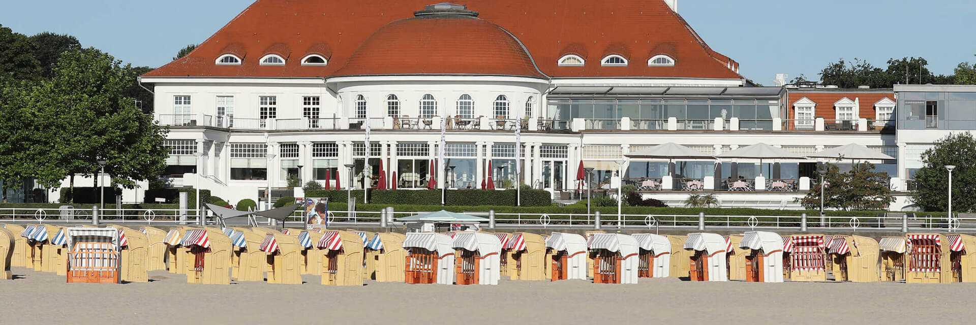 ATLANTIC Grand Hotel Travemünde with red roof, beach chairs on the sandy beach, sea in the foreground.
