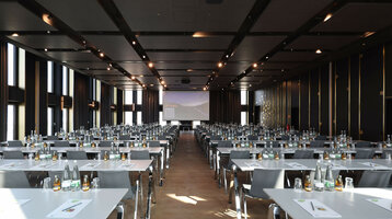 Modern conference room at the ATLANTIC Hotel Heidelberg with tables, chairs and presentation screen.