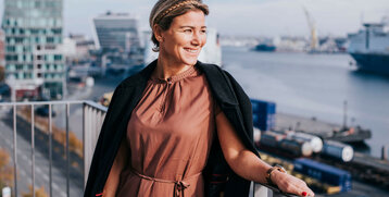 Frau auf Hotelbalkon mit Blick auf Kieler Hafen, lächelnd, bei sonnigem Wetter.