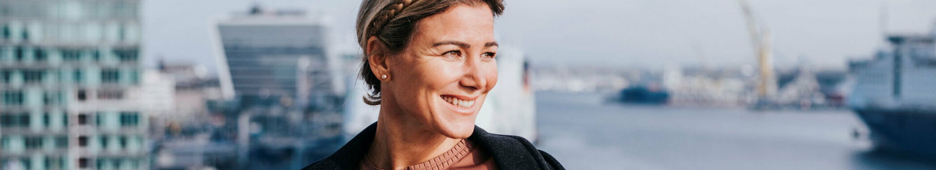 Eine Frau steht auf ihrem Zimmerbalkon und schaut lächelnd in die Sonne.