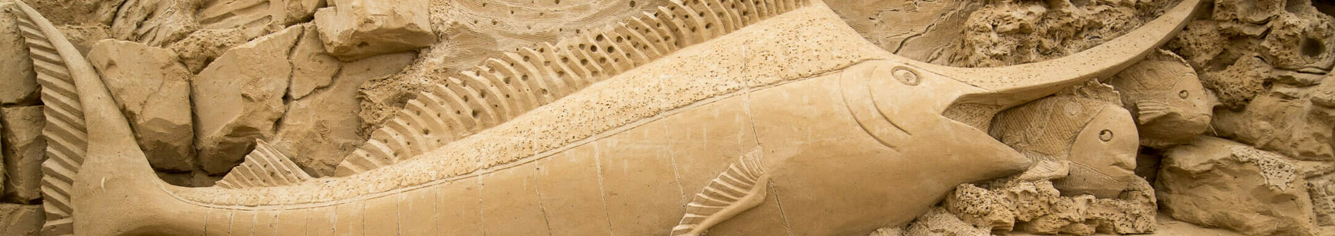 Sandskulpturen-Festival Sandsteinrelief mit detailreichem Schwertfisch und Meeresmotiven in Travemünde.