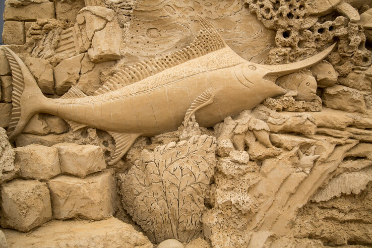 Sandsteinrelief mit detailreichem Schwertfisch und Meeresmotiven in Travemünde.