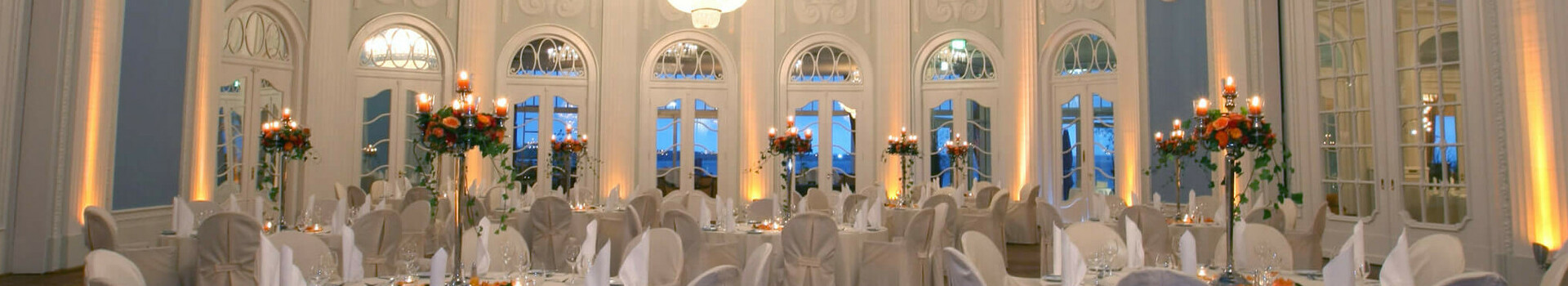 Ballsaal im ATLANTIC Grand Hotel Travemünde Eleganter Ballsaal im ATLANTIC Grand Hotel Travemünde mit runden, gedeckten Tischen und prächtigem Kronleuchter.
