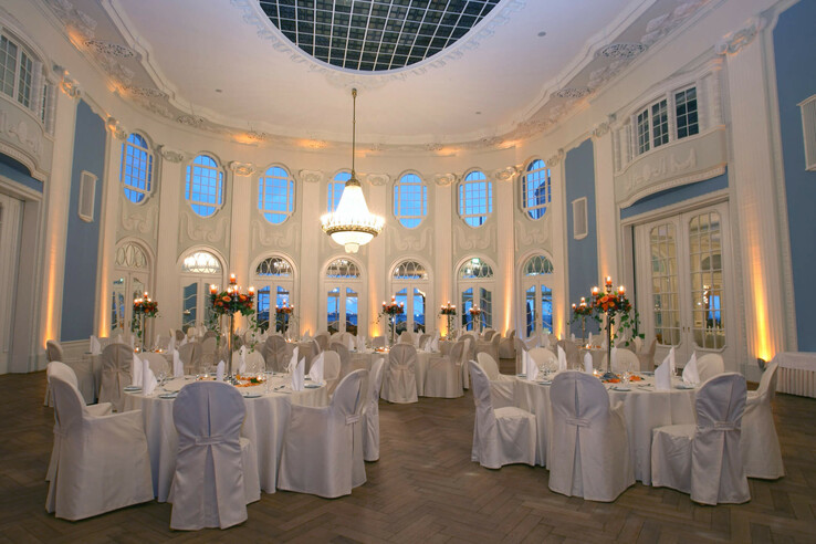 Elegant ballroom in the ATLANTIC Grand Hotel Travemünde with round, laid tables and a magnificent chandelier.