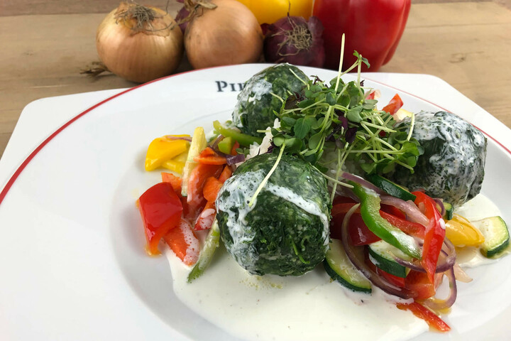 Three spinach dumplings with colorful peppers and zucchini on a white sauce, decorated with fresh herbs.