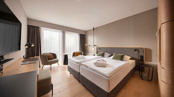 Modernes Hotelzimmer mit Doppelbett, Schreibtisch, Sessel und großem Fenster mit Vorhängen im ATLANTIC Hotel Heidelberg.