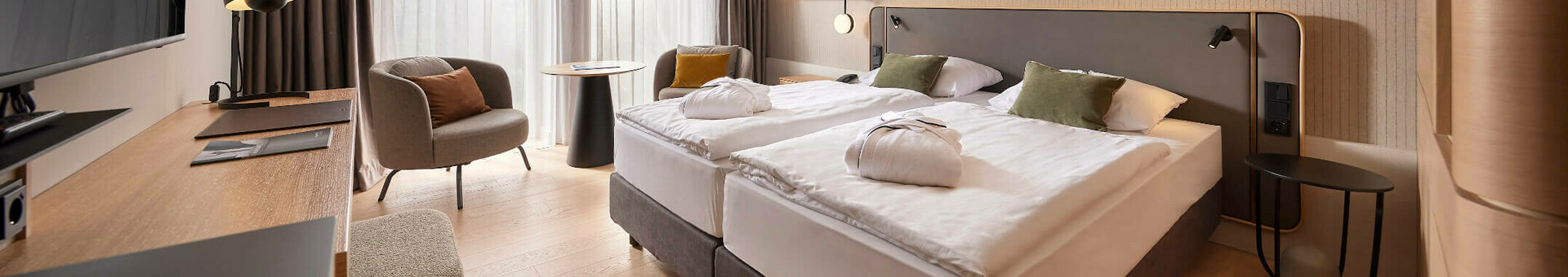 Modernes Hotelzimmer mit Doppelbett, Schreibtisch, Sessel und großem Fenster mit Vorhängen im ATLANTIC Hotel Heidelberg.