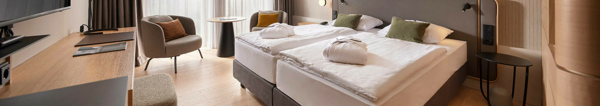 Modern hotel room with double bed, desk, armchair and large window with curtains at the ATLANTIC Hotel Heidelberg.