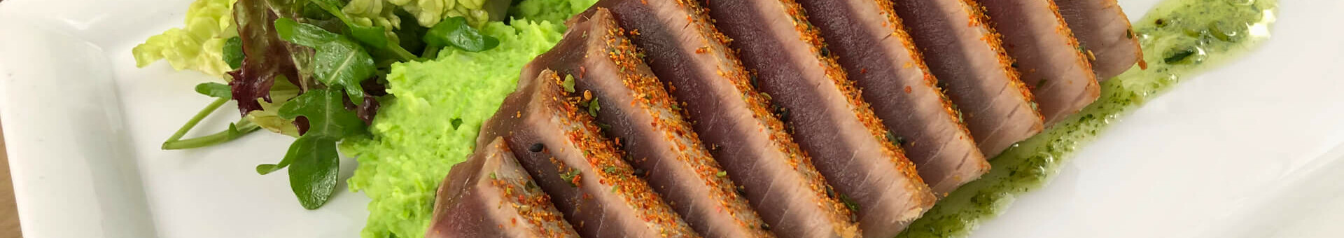 A plate of thinly sliced tuna, green puree and fresh salad.