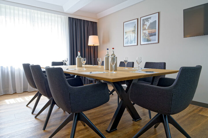 Modern conference room at the ATLANTIC Hotel Landgut Horn with large table, eight chairs, water bottles and glasses.