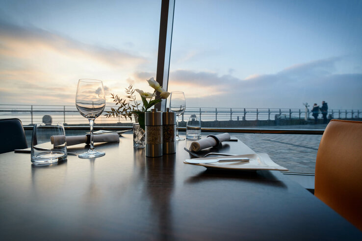 Elegant table setting at the ATLANTIC Hotel Sail City, Bremerhaven, with a view of the promenade at sunset.