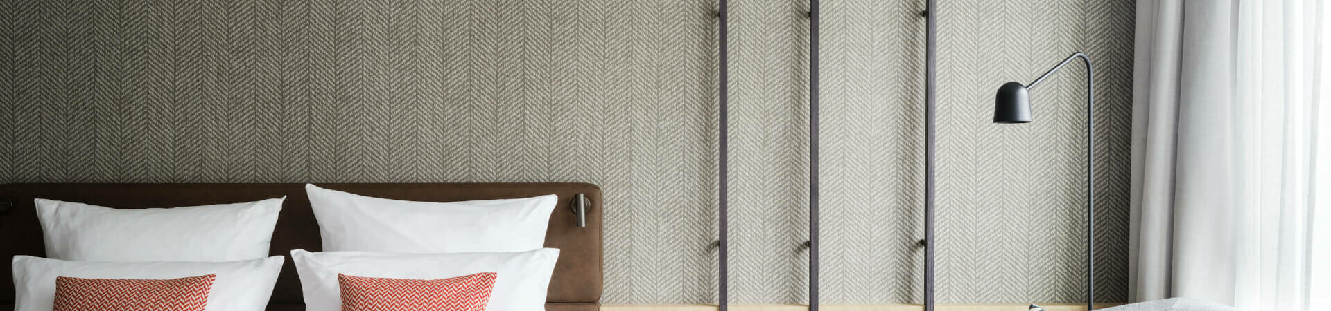 Zimmer Comfortplus im ATLANTIC Hotel Münster Modernes Hotelzimmer mit Doppelbett, grauem Sofa, dekorativen Kissen und stilvoller Wandgestaltung mit Fahrraddeko.