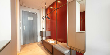 Moderner Flur im ATLANTIC Grand Hotel Bremen mit roter Wand, Kleiderstange, Sitzbank und großem Spiegel.