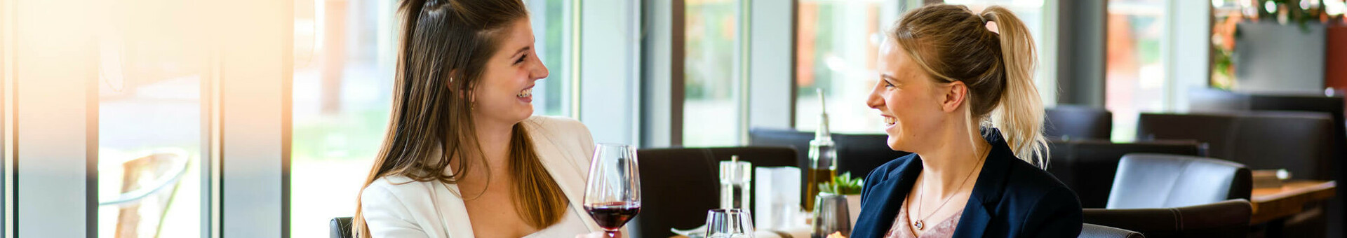 Gäste im Restaurant| Restaurant CAMPUS im ATLANTIC Hotel Universum Zwei Frauen sitzen im Restaurant des ATLANTIC Hotel Universum, lächeln und stoßen mit Rotwein an.